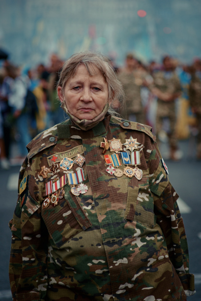 Une femme soldat ukrainienne d’âge moyen regarde la caméra ; elle a de nombreuses médailles sur sa veste.